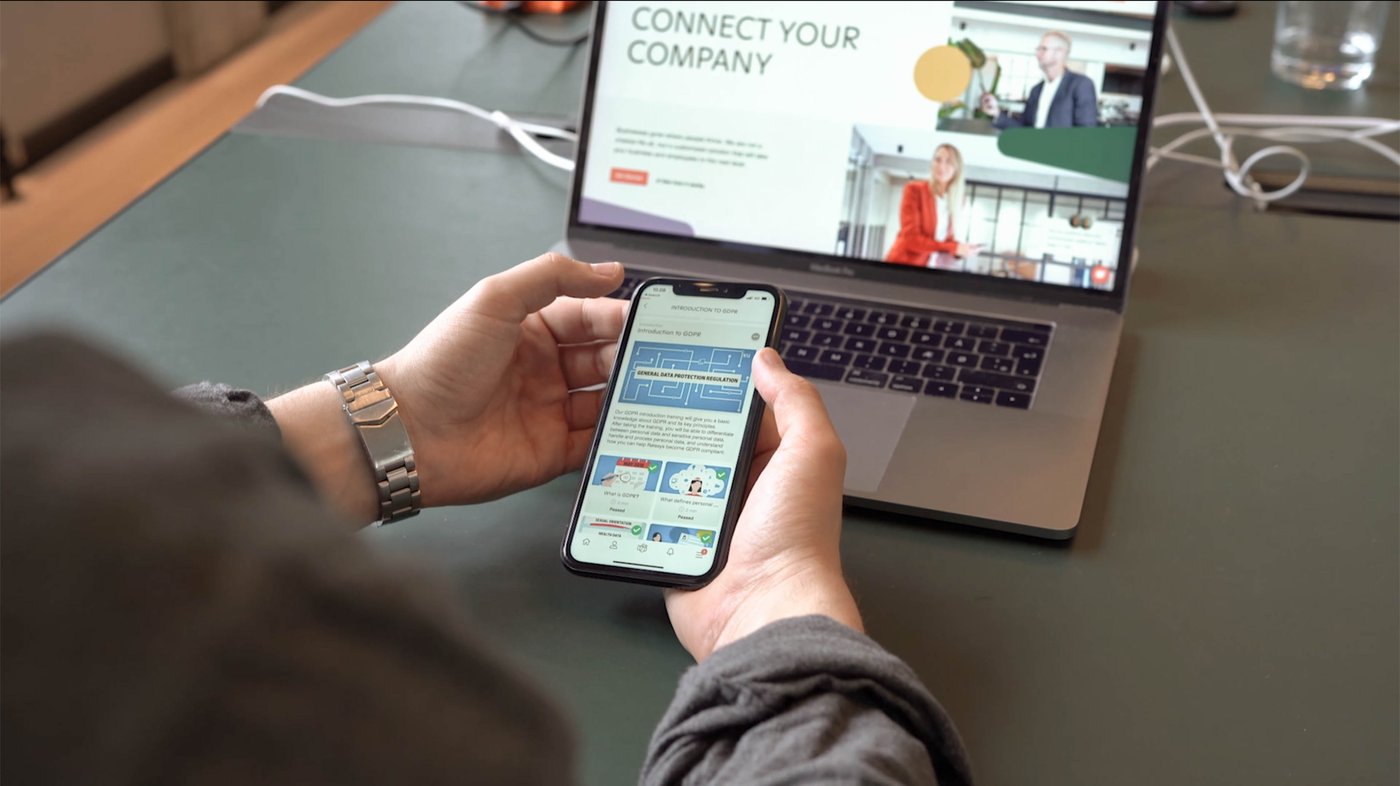 Image of a person wearing a watch holding a mobile phone with a laptop open next to it